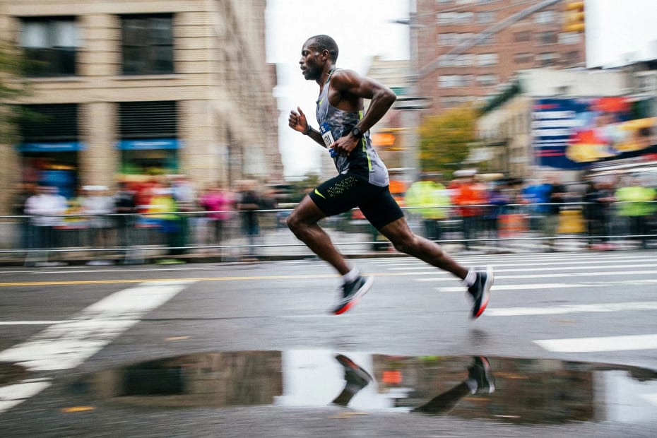 Runner in azione dinamica durante una gara, con effetto mosso che enfatizza la velocità e riflesso nell'acqua.