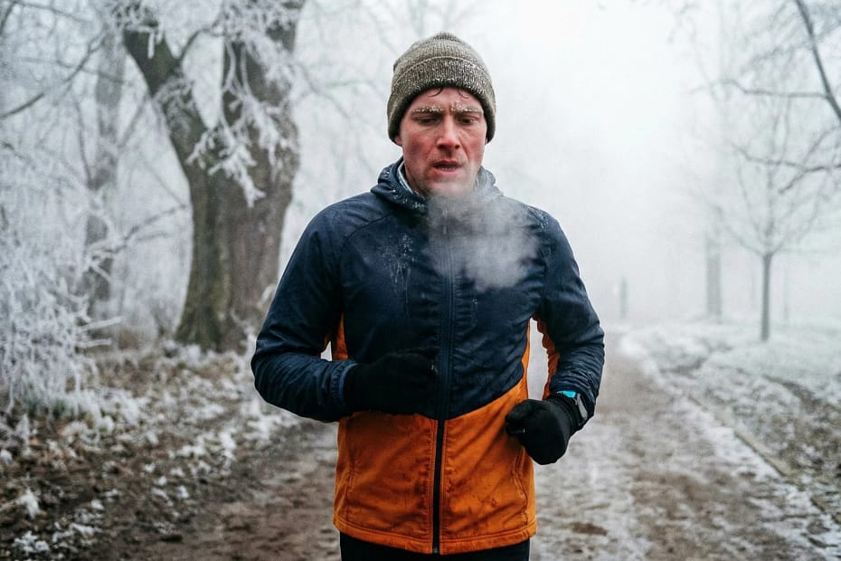 Runner in abbigliamento termico corre in un parco ghiacciato con respiro visibile, immagine rappresentativa per l'allenamento invernale di corsa e la costruzione della base aerobica.